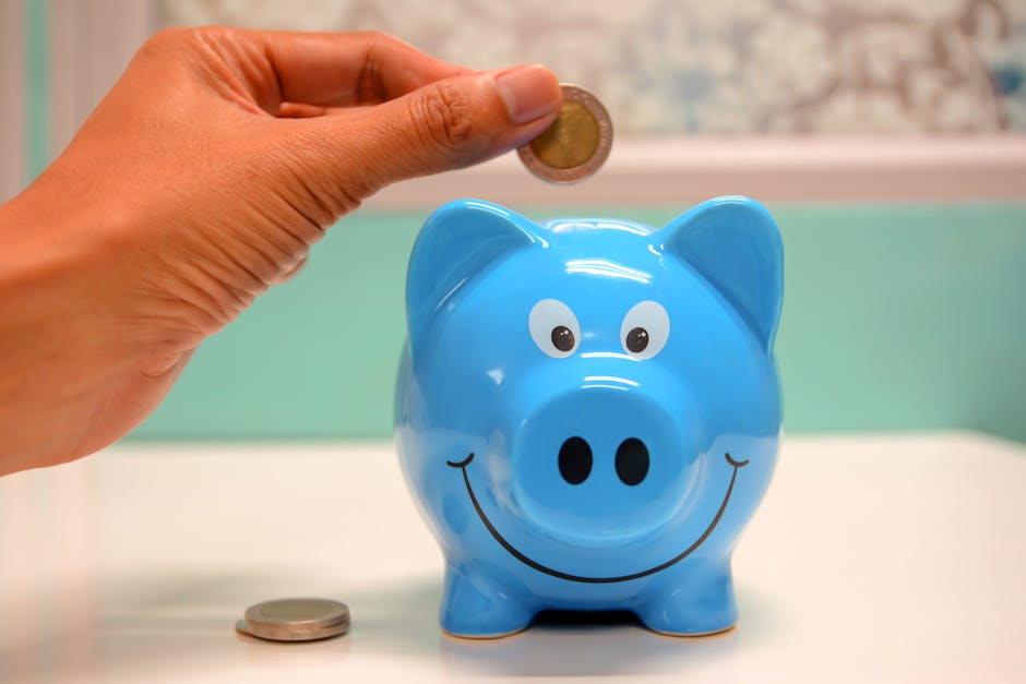 Hand inserting a coin into a blue piggy bank for savings